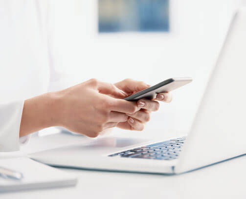 Image of person’s hands making a phone call while looking at laptop